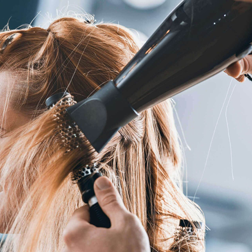 Immagine di una mano di una parrucchiera che sta utilizzando il phon per asciugare dei capelli